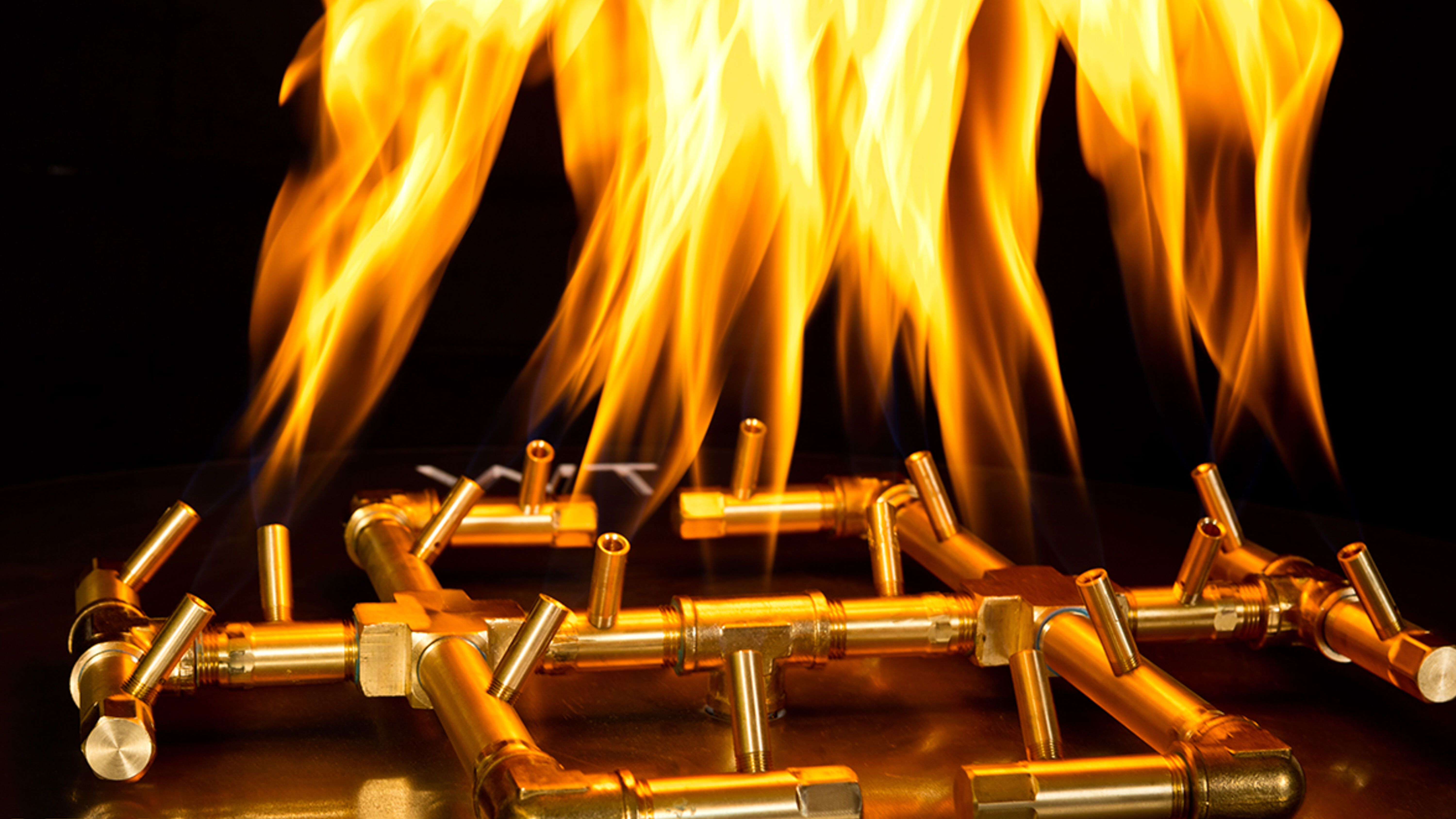 A close-up view of a brass CrossFire gas fire pit burner and supercharged orange flames.